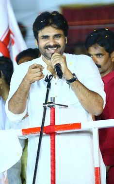 a man standing in front of a cross holding a microphone and wearing a white shirt