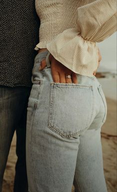 a man and woman standing next to each other on the beach with their hands in their pockets