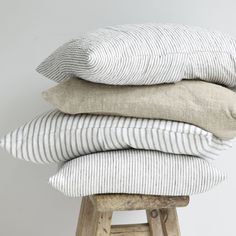 three pillows stacked on top of each other in front of a white wall and wooden stool