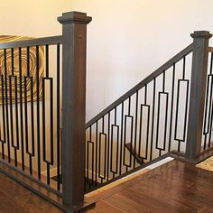 an iron stair railing with wooden handrails in a home setting, next to a white wall and hardwood flooring