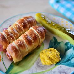 two hotdogs on a plate with mustard and pickle slices next to them