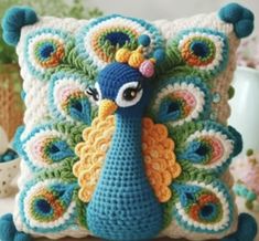 a crocheted peacock pillow sitting on top of a table next to a vase