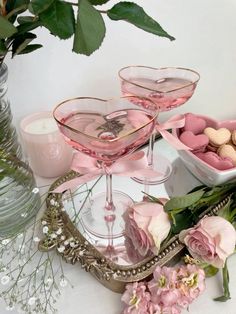 two martini glasses filled with pink candy and flowers on a table next to some vases