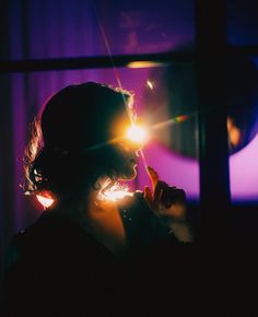 a woman holding a sparkler in front of her face while looking out the window