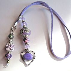 two necklaces with beads and charms hanging on a purple cord next to each other