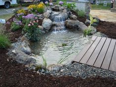 a small pond in the middle of a garden with rocks and flowers around it, along with a wooden deck