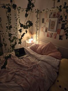 an unmade bed with ivy growing on the wall above it and a laptop computer sitting on top