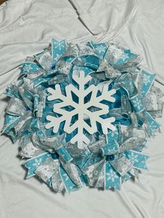 a snowflake wreath made out of blue and silver ribbons on a white sheet