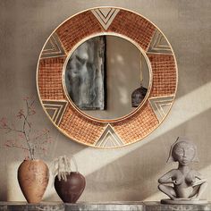 a round mirror sitting on top of a shelf next to vases and a statue