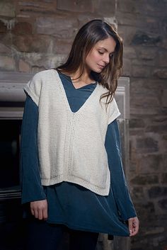 a woman standing in front of a brick wall wearing a sweater and leggings