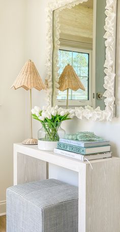 a white table topped with books and a vase filled with flowers next to a mirror