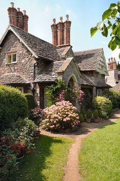 a stone house surrounded by lush green grass and flowers in the front yard with a path leading to it