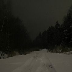 a person riding skis down a snow covered road in the woods at night time