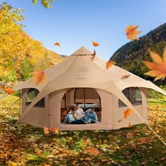 two people sitting in a tent on the ground with autumn leaves surrounding it and mountains in the background