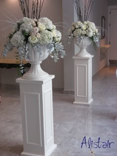 two white vases with flowers in them are on display at the entrance to an event