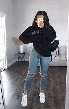 a woman taking a selfie while wearing ripped jeans and a black sweatshirt with the words,