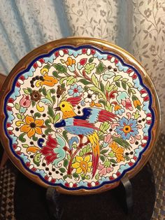 an ornately decorated plate sitting on top of a wooden table next to a curtain