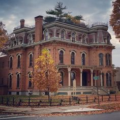 an old brick building with many windows and balconies on the top floor is surrounded by autumn leaves