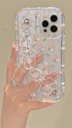 a hand holding up a clear case with flowers on it and two rings attached to the back