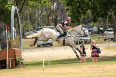 a woman riding on the back of a white horse over an obstacle in a park