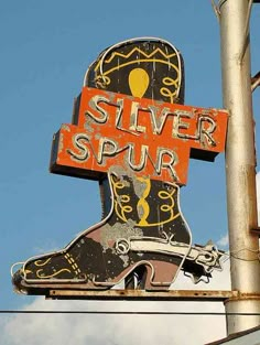 an old silver spur sign hanging off the side of a pole in front of a blue sky