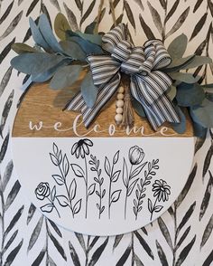 a wooden sign that says welcome with flowers and leaves on the front, hanging on a zebra print wall