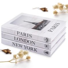 three books sitting next to each other on top of a white table with dried flowers