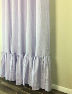 a cat sitting on top of a wooden floor next to a window with purple curtains