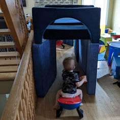 a toddler sitting on a stool in front of a play house with stairs leading up to the second floor