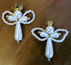 two white angel brooches with pearls on them sitting on a wooden table next to each other