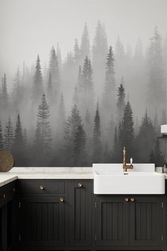 a kitchen with black cabinets and a white sink in front of a forest wall mural