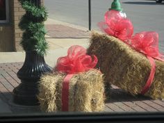 two hay bales wrapped in red ribbon and tied to a lamp post on the sidewalk