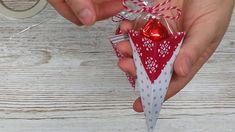 a person holding a red and white ornament in their hand on a wooden table