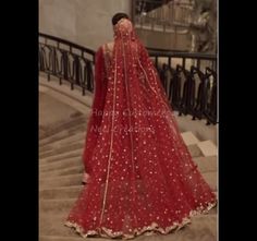 a woman in a red bridal gown standing on stairs with her veil draped over her head