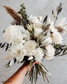 a bouquet of white flowers in someone's hand with feathers on the side and greenery