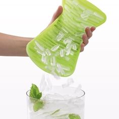 a person is holding a green strainer over ice cubes with mint leaves on top