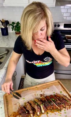 a woman in the kitchen eating some food on a cutting board with a knife and fork