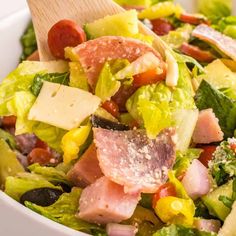 a salad with ham, lettuce, tomatoes and olives in a white bowl