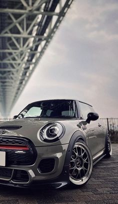 a grey mini cooper parked under a bridge