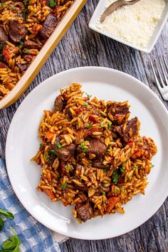 a white plate topped with meat and rice next to a casserole dish on a wooden table