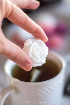 a person is dipping something into a cup of hot chocolate in the shape of a flower