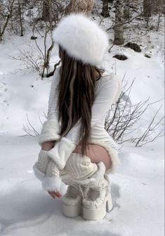 a woman with long hair wearing white boots and a fur hat sitting in the snow