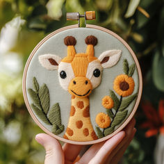 a hand holding up a small embroidered giraffe with flowers on it's face