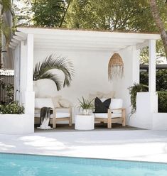 an outdoor living area next to a pool with white furniture and palm trees in the background