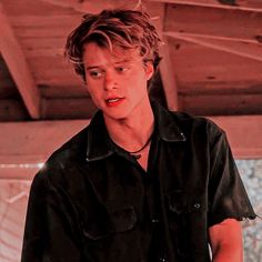 a young man in black shirt standing next to a white wall and looking at the camera