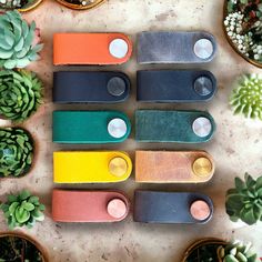 several different colors of leather keychains sitting next to succulents