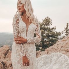 a woman standing on top of a mountain wearing a white wedding dress with long sleeves