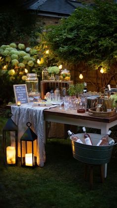 an outdoor dinner table with candles and lights on the outside, surrounded by greenery