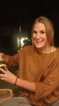 a woman sitting on the ground holding a can in her hand and smiling at the camera