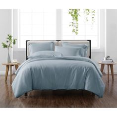 a bed with blue sheets and pillows in a room next to a table, potted plant and window